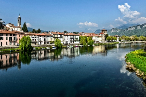 Immagine con fiume, alberi, riflessi, case, acqua, campanile, riflesso, nuvole, verde, panorama, monti