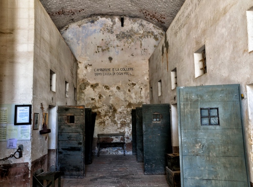 Immagine con porte, finestre, carcere, quadro, celle, legno, catena, panchina, panca, pareti, arco, grate, stanza, scritta, abbandono