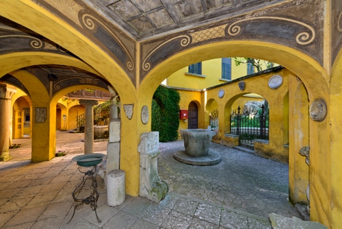 Immagine con pozzo, archi, giallo, portico, portici, catino, colonne, affreschi, cancello, cortile, pilastri