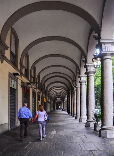 Immagine con archi, colonne, portico, coppia, due, passanti, donna, uomo, persone, serrande, portici