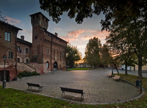 Immagine con panchine, castello, alberi, piazza, torre, tramonto, lampione