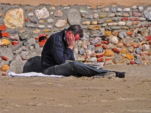 Immagine con muro, sabbia, leggere, spiaggia, pietre, sassi, giornale, uomo, seduto, persona