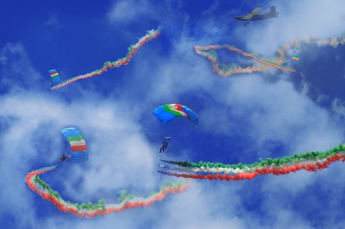 Immagine con cielo, nuvole, tricolore, scie, paracadute, bianco, azzurro, rosso, verde, paracadutisti, aereo, paracaduti, fumo, colori