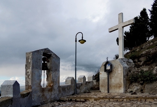 Immagine con campana, lampione, croce, alberi, nuvole, cielo, cimitero, merli, monumento, campanile