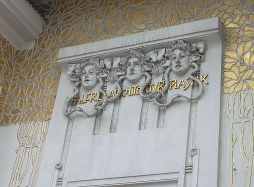 Immagine con oro, liberty, serpenti, mascheroni, foglie, tre, scritte, scritta, dorato, palazzo, facce, decorazioni, maschere, lettere, volti, visi