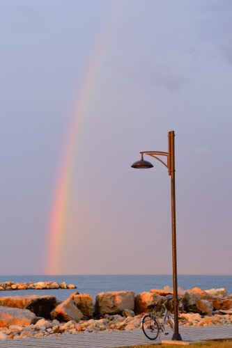Immagine con arcobaleno, mare, bicicletta, lampione, scogli, cielo
