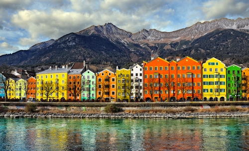 Immagine con fiume, colori, acqua, montagne, case, giallo, palazzi, arancione, verde