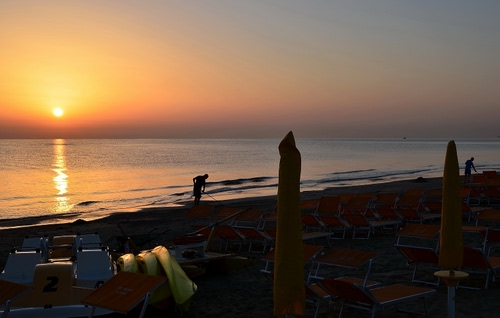 Immagine con tramonto, mare, spiaggia, sole, ombrelloni, acqua, lettini, cielo, sdraio