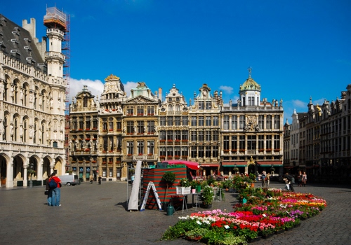 Immagine con piazza, fiori, palazzi, persone, colori, finestre, piante, passanti