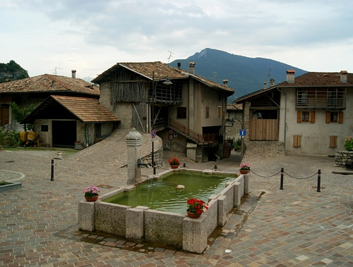 Immagine con fontana, piazza, montagna, case, acqua, paese, fiori, borgo, vasi
