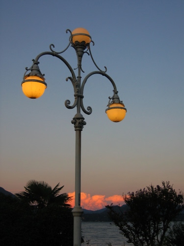 Immagine con lampione, alberi, nuvole, cielo, tramonto, acqua, tre, palo, luci, luce, sfere, lampioni, palle, montagne, palma, lago