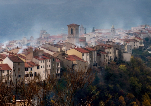 Immagine con case, alberi, tetti, nebbia, paese, campanile, torre, fumo, foschia, borgo