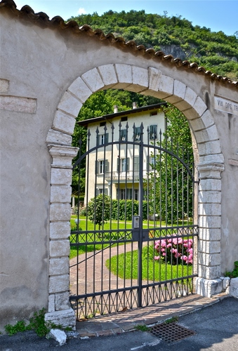 Immagine con cancello, fiori, arco, villa, verde, giardino, finestre, tombino, erba, aiuole, alberi, ferro, piante, prato, muro, palazzo, cielo, collina, rosa