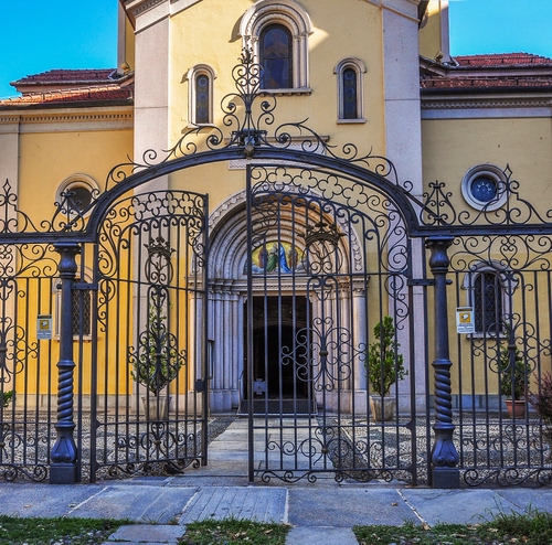 Immagine con cancello, chiesa, ferro, portone, finestre, giallo, porta, ingresso, piante, arco, archi, lunetta