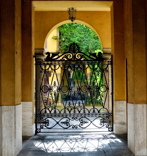 Immagine con cancello, ferro, arco, ingresso, giallo, ombra, verde, lampada, pilastri, colonne, piante