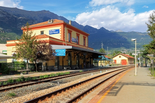 Immagine con stazione, montagne, binari, cielo, alberi, nuvole, ferrovia, lampioni, rotaie, lampione, case, azzurro, finestre, pensilina, montagna