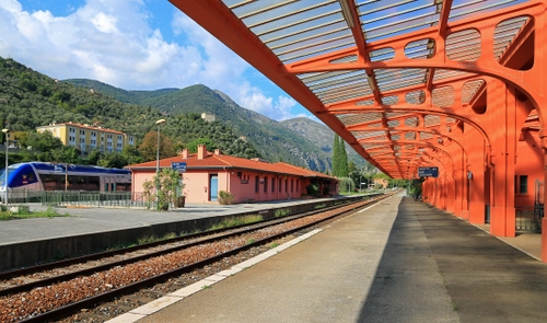 Immagine con stazione, treno, binari, pensilina, rosso, binario, montagne, arancione
