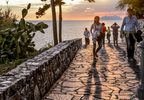 Immagine con mare, isola, persone, tramonto, passanti, ombre, passeggiata, muretto, turisti, cactus
