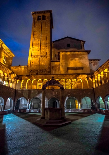 Immagine con pozzo, archi, chiesa, torre, luci, chiostro, notte, campanile, piazza, colonne, notturno, ombre, portici, convento, case, porticato, cielo, giallo, finestre