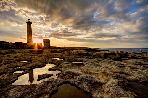 Immagine con faro, nuvole, tramonto, cielo, riflesso, mare, rocce, scogli, sole, acqua