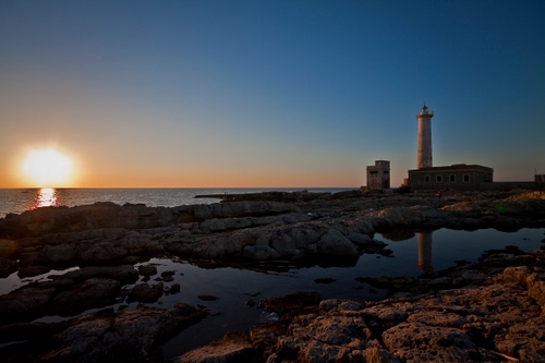 Immagine con mare, tramonto, faro, sole, scogli, riflesso, acqua, cielo