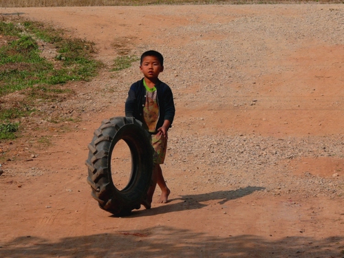 Immagine con bambino, ruota, terra, ombra, erba, verde, gomma, cerchio, giocare, scalzo, gioco