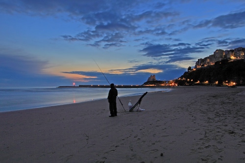 Immagine con mare, pescatore, spiaggia, tramonto, luci, canna, case