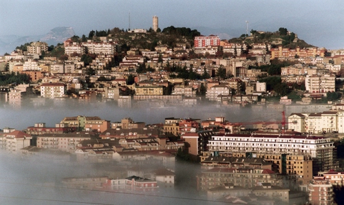Immagine con città, nebbia, panorama, torre, palazzi, case, collina, foschia, cielo, alberi, gru, paese, borgo