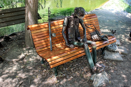 Immagine con panchina, statua, pescatore, albero, canna, legno, acqua, cappello, parco, gatto, strada, tronco, cestino