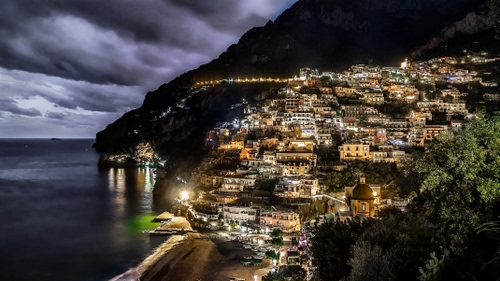 Immagine con mare, nuvole, luci, borgo, cielo, spiaggia, alberi, panorama, notturno, case, notte, paese, costa, acqua, riflessi, chiesa