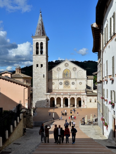 Immagine con chiesa, campanile, persone, piazza, nuvole, cielo, scalinata, archi, duomo, case, rosone, finestre, spoleto, umbria, scale, portico, azzurro, fiori