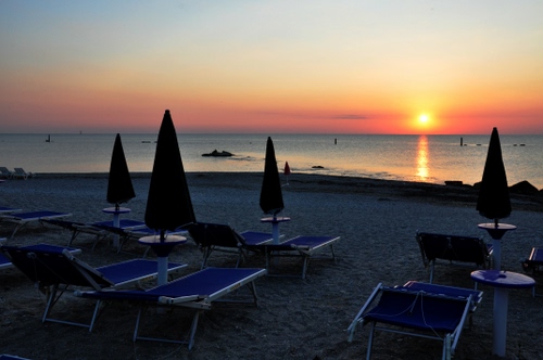 Immagine con ombrelloni, spiaggia, tramonto, mare, lettini, sole, sdrai, controluce