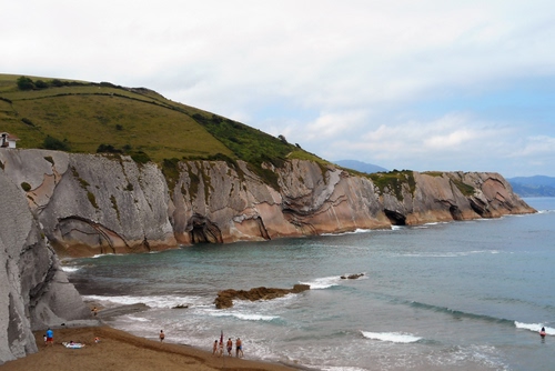 Immagine con mare, spiaggia, scogliera, sabbia, cielo, acqua, persone, nuvole, onde, scogli, bagnanti, costa, azzurro, roccia, verde, montagna