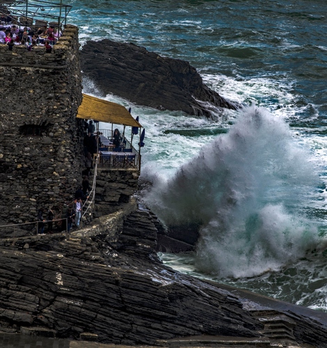 Immagine con mare, onde, schiuma, onda, scogliera, tettoia, rocce, persone, scogli, terrazza, mareggiata, bianco, costa, tavolini, tenda, parapetto, acqua, ombrelloni, roccia, ringhiera