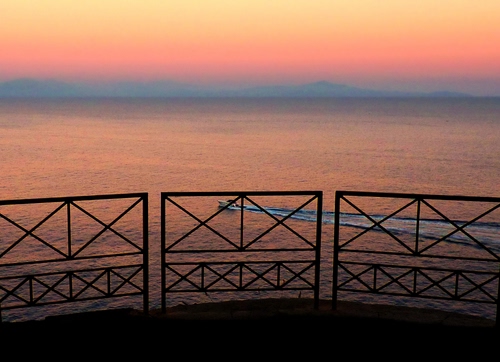 Immagine con tramonto, mare, barca, ringhiera, scia, rosso, motoscafo, acqua, cielo, rosa, terrazza, riflesso, riflessi, imbarcazione