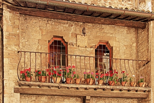 Immagine con fiori, balcone, finestre, ringhiera, vasi, rosso, tetto, verde, tegole, mattoni, terrazza, gerani, palazzo, grondaia, ferro, lampada, due