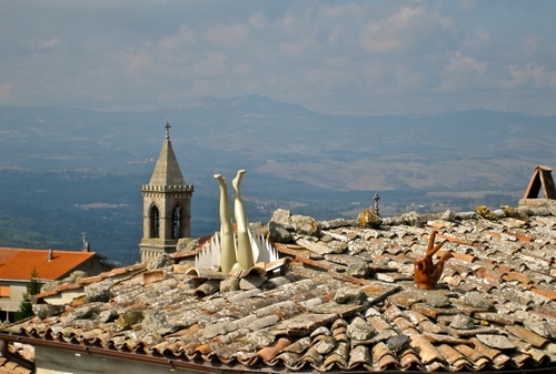 Immagine con campanile, gambe, tetti, mano, tegole, panorama, tetto, coppi, nuvole, cielo, montagne, manichino, pietre, comignolo, foschia, arte, croce