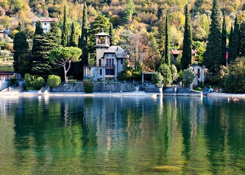 Immagine con lago, alberi, acqua, riflessi, villa, cipressi, verde, torre, riflesso, case, bosco, finestre, barche, casa