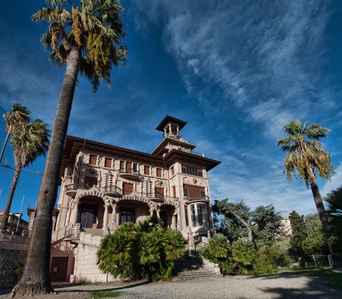 Immagine con palme, villa, alberi, nuvole, cielo, finestre, archi, verde, casa, azzurro, scalinata, balconi, scale, torretta, liberty, palazzo, torre, altana