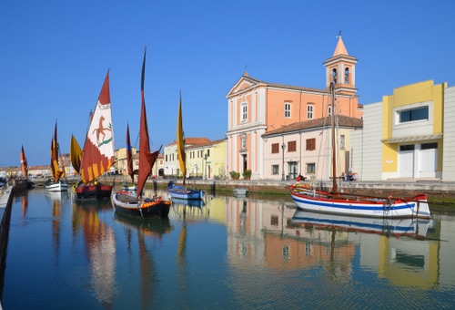 Immagine con chiesa, vele, barche, acqua, canale, cielo, campanile, case, riflesso, azzurro, riflessi, finestre, fiume, vela, cesenatico