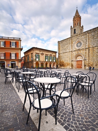 Immagine con chiesa, sedie, piazza, tavolini, rosone, campanile, nuvole, cielo, finestre, palazzi, case, archi, cubetti, bar, porte, tavoli, selciato, porfido, balconi