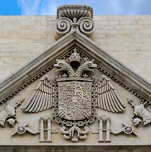 Immagine con stemma, ali, triangolo, aquila, corona, simboli, teste, colonne, muro, cannoni, cielo, bassorilievo, croce, marmo, scudo, due