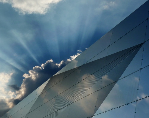 Immagine con nuvole, raggi, cielo, riflesso, azzurro, vetro, palazzo, triangolo, geometria, luce, sole, controluce, riflessi, diagonale