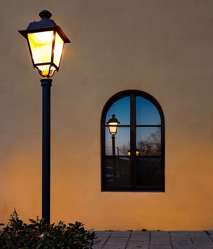 Immagine con lampione, finestra, luce, riflesso, muro, arco, vetro, riflessi, palo, cespuglio, notte, acceso, strada, azzurro, cielo, giallo, arancione