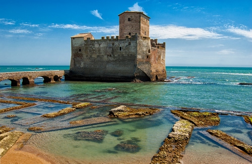 Immagine con castello, nuvole, mare, torre, cielo, ponte, azzurro, acqua, merli, verde, bianco, ruderi, archi, mura